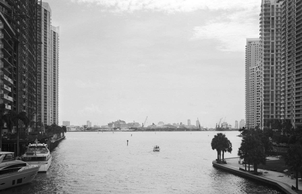the mouth of the Miami river where it flows into Biscayne Bay with apartments and offices in Black and white. With only 5.5 miles, the Miami River is the shortest working river in the US. There are sever small cargo terminals where small cargo ships loads goods for shipments to the Bahamas and several Caribbean Islands. Before "civilization" kicked in, the river was home to the Mayaimi, which means "Sweet Water" (hence the current name Miami) and the Tequesta Indians This image was captured with a 1937 Zeiss Ikon Rangefinder camera