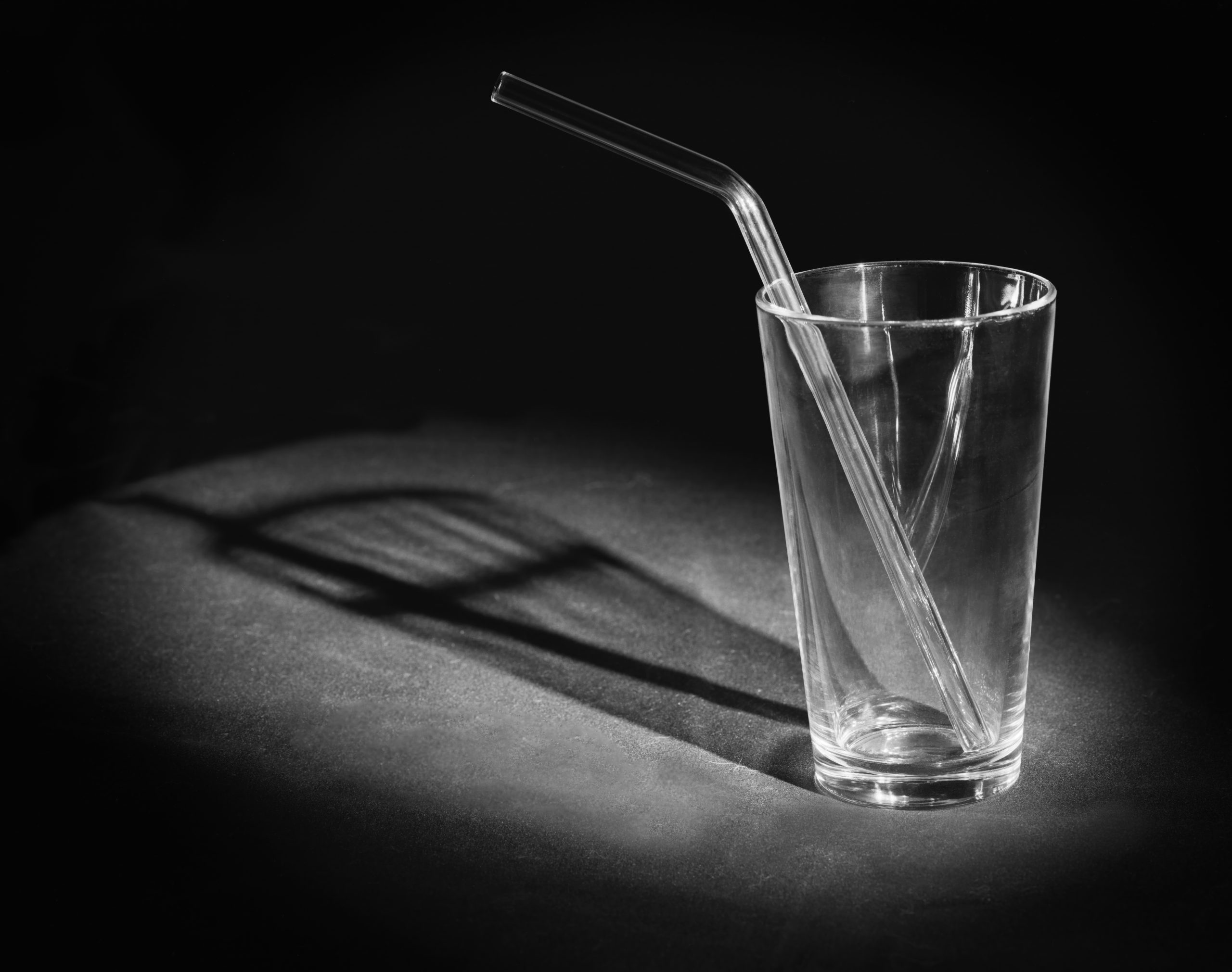 Studio capture of an empty glass and a glass straw with deep shadows. The emptiness of the glass is up to the interpretation of the viewer. Captured on 4 x 5 " B/W sheet film. Home processed